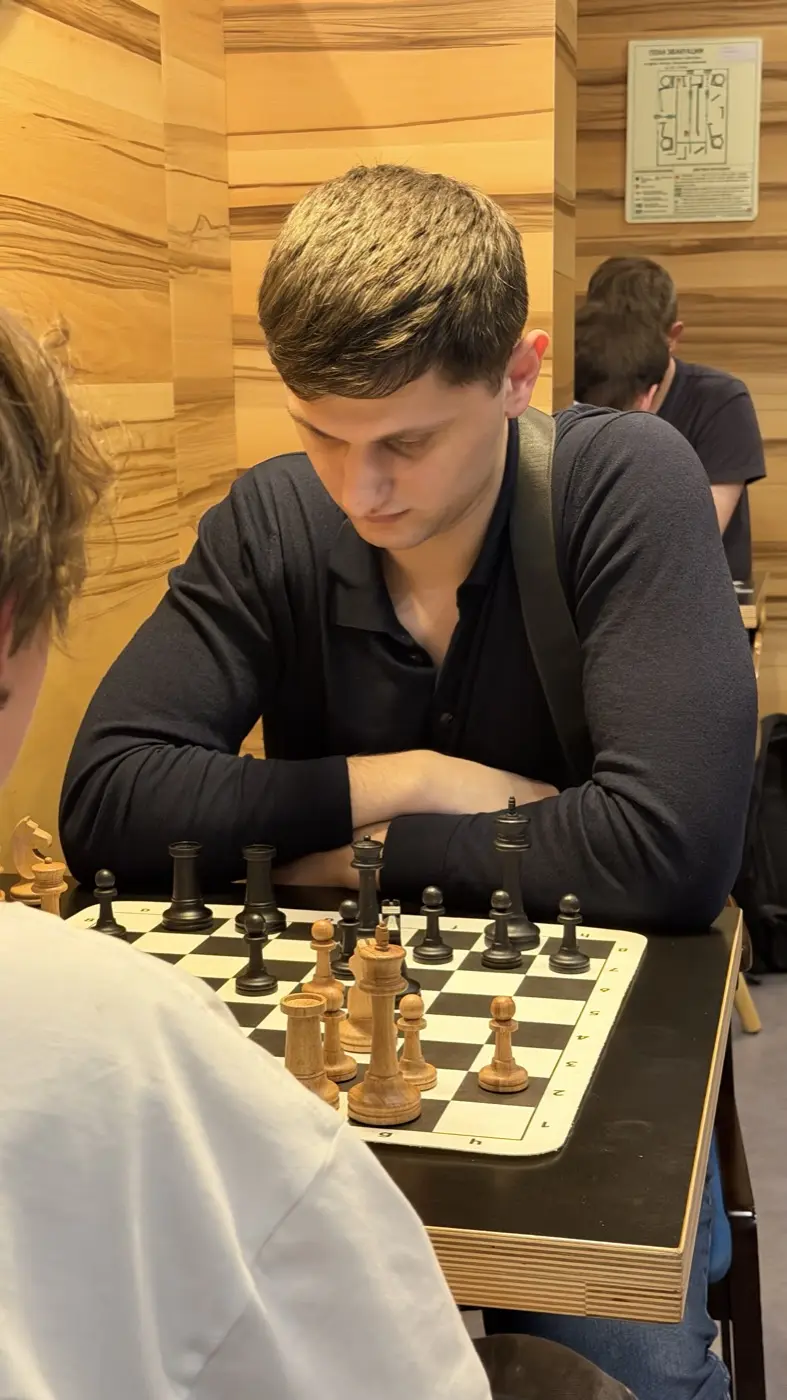 A player in a dark shirt over the board, arms crossed