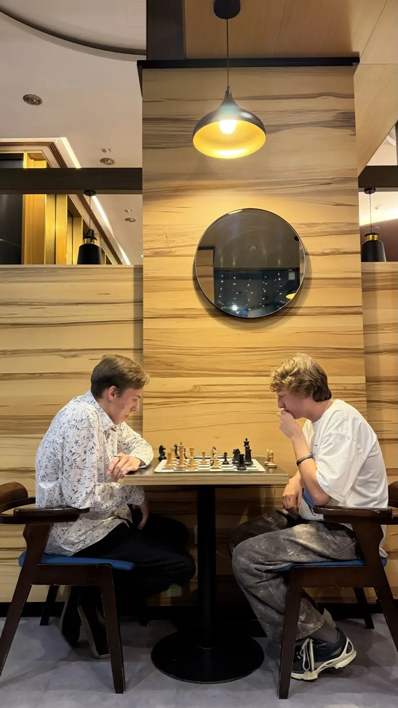 Two people playing at a round table under a lamp by a wooden wall