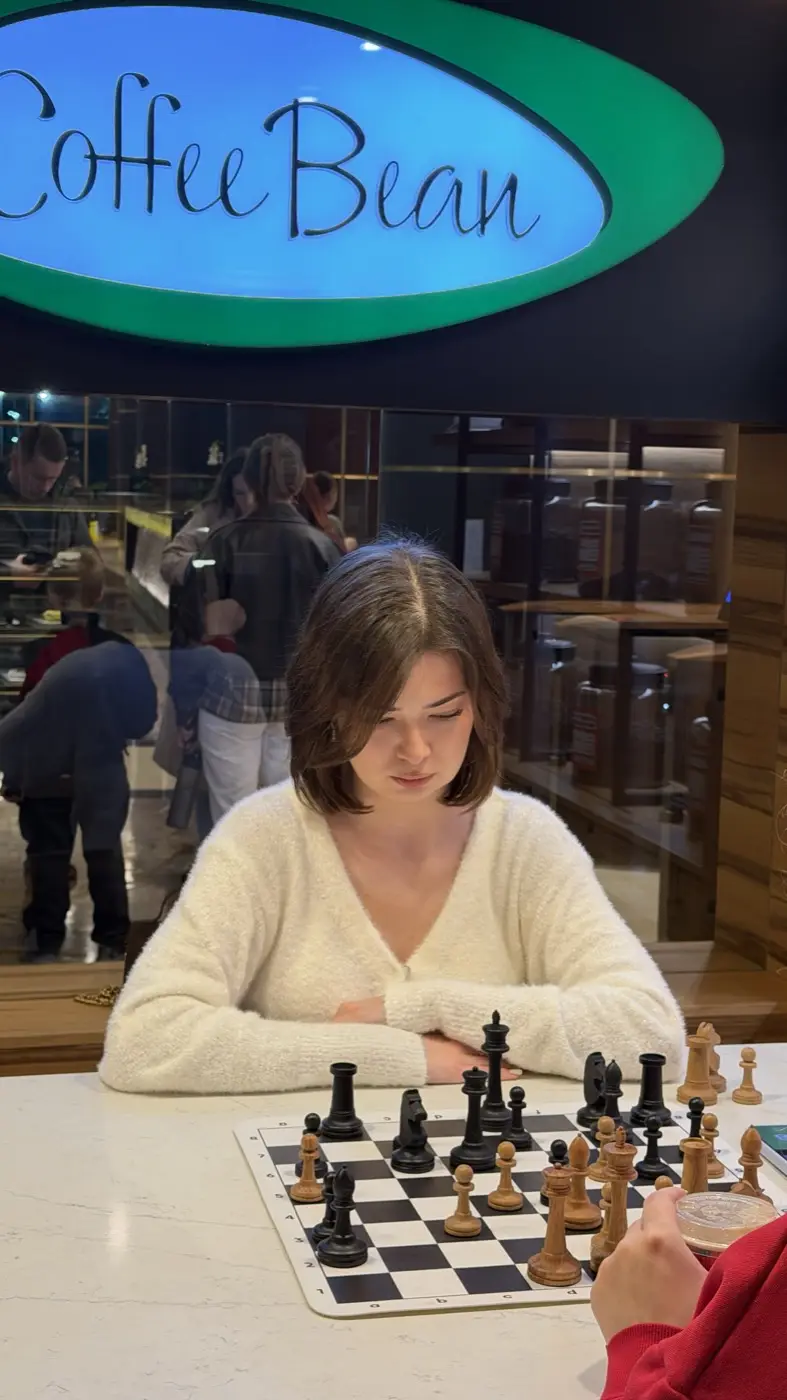 A player in a white sweater over the board, the Coffee Bean sign behind her