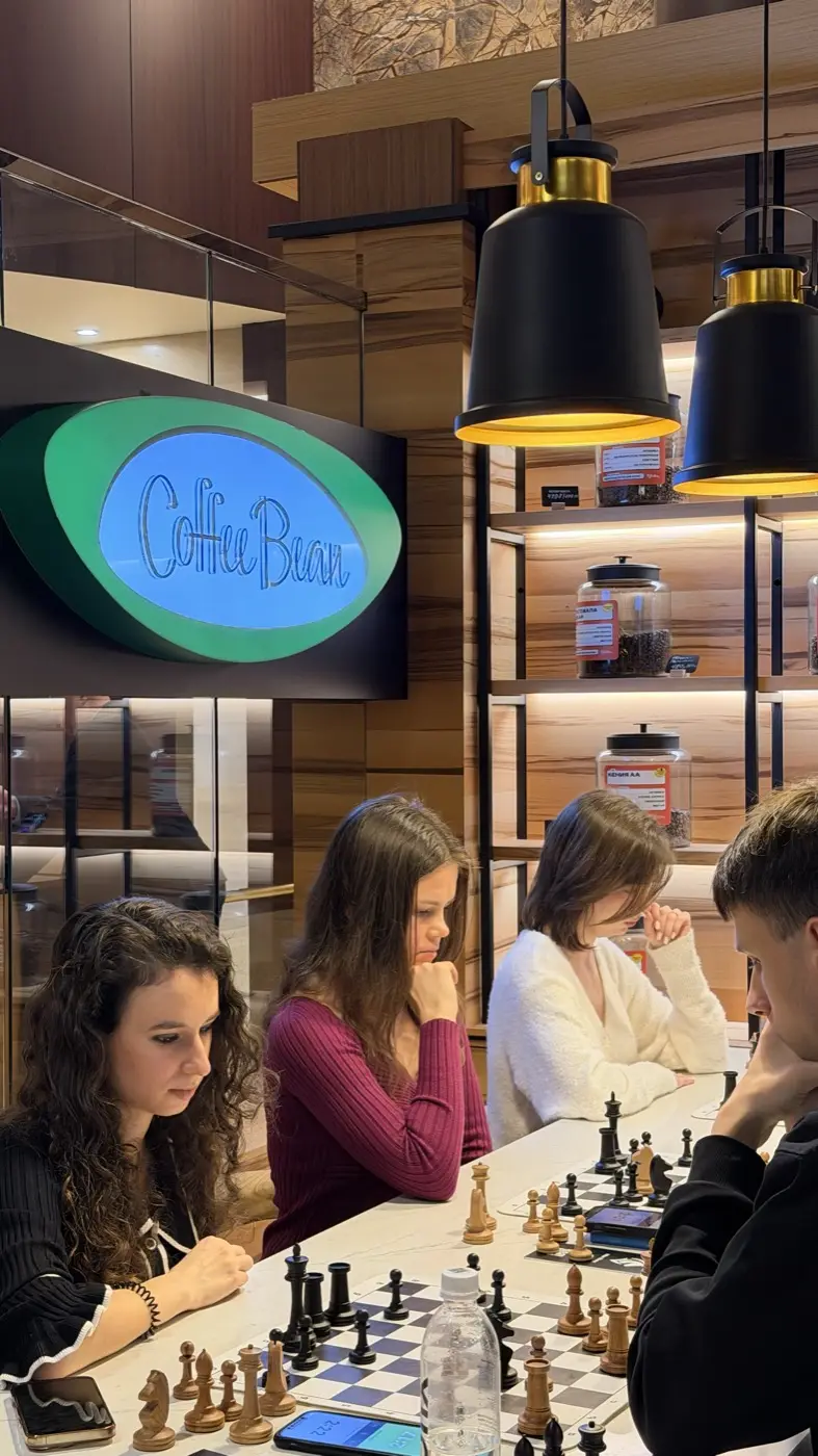 Three players at a long table under lamps, a Coffee Bean sign on the wall