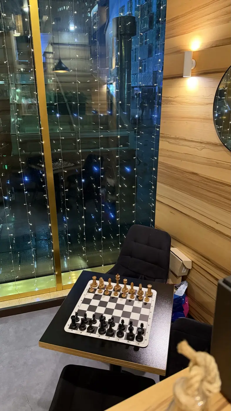 A board with the pieces set up by the window, the night lights of Moscow City behind the glass