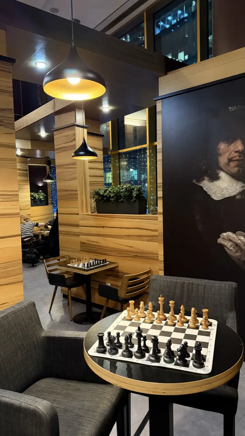 A board with pieces in the foreground, more tables with boards deeper in the room