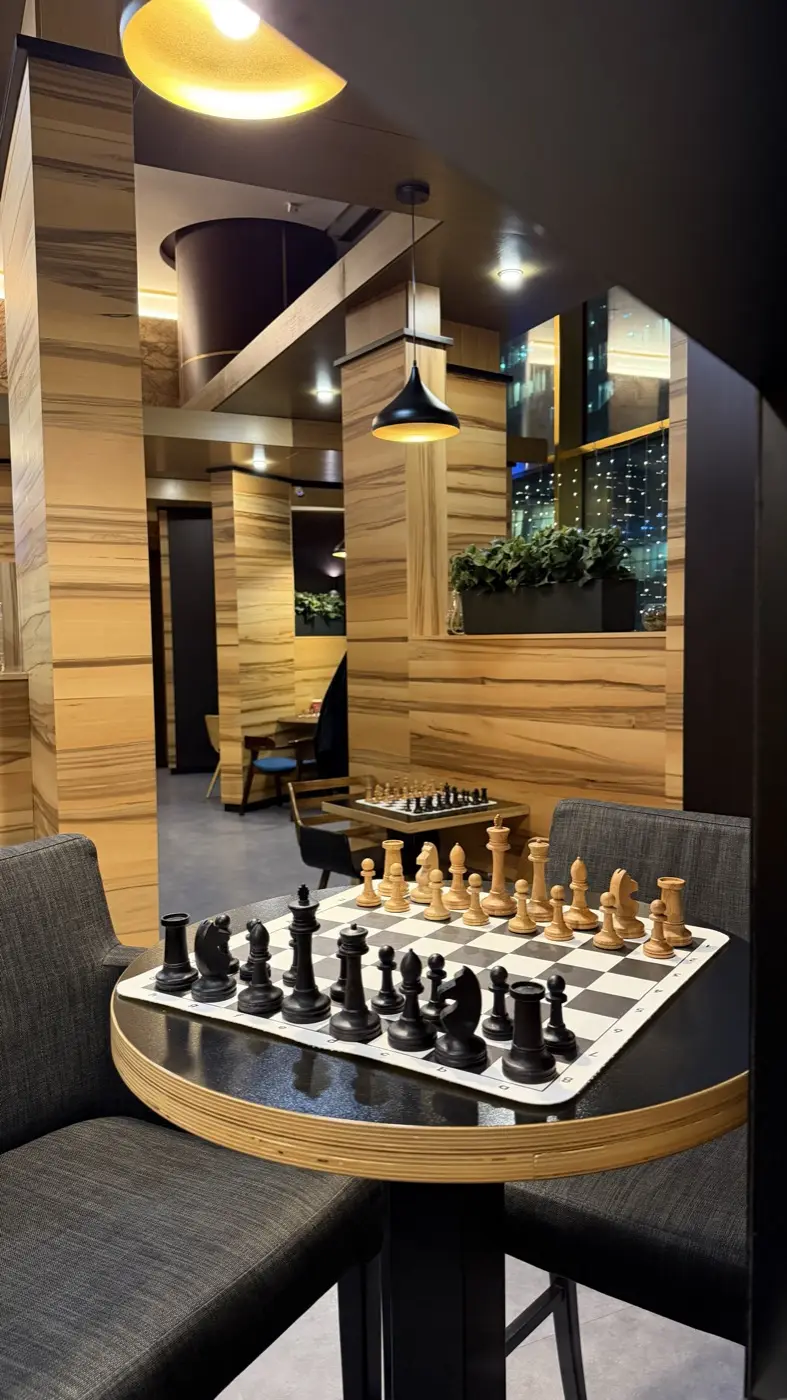 A round table with a chess set under a yellow lamp, columns deeper in the room