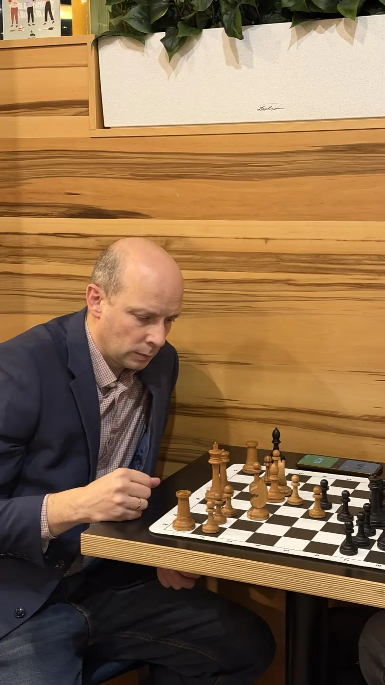 A player in a jacket making a move on a chessboard in a coffee shop